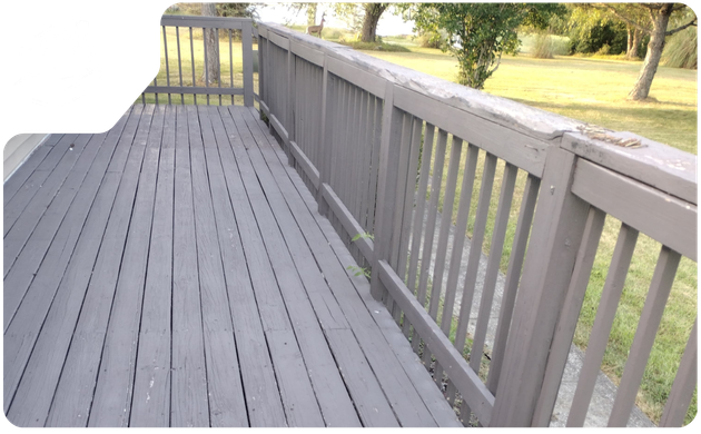 Empty grey painted wooden deck with matching wooden railings overlooking a green grassy backyard with trees.